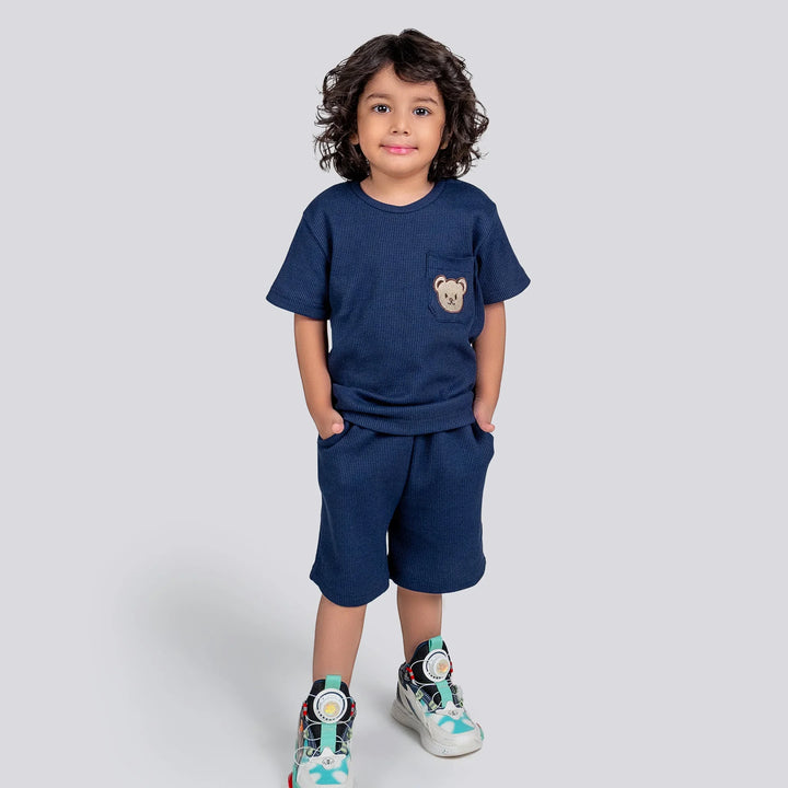 Child wearing a navy blue outfit with a bear emblem on a plain background