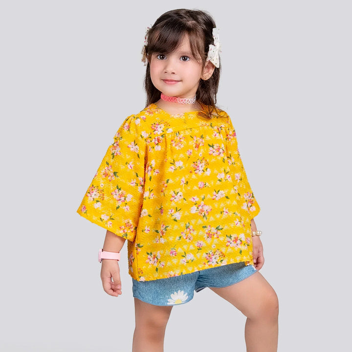 Child wearing a yellow floral blouse and denim shorts on a light gray background