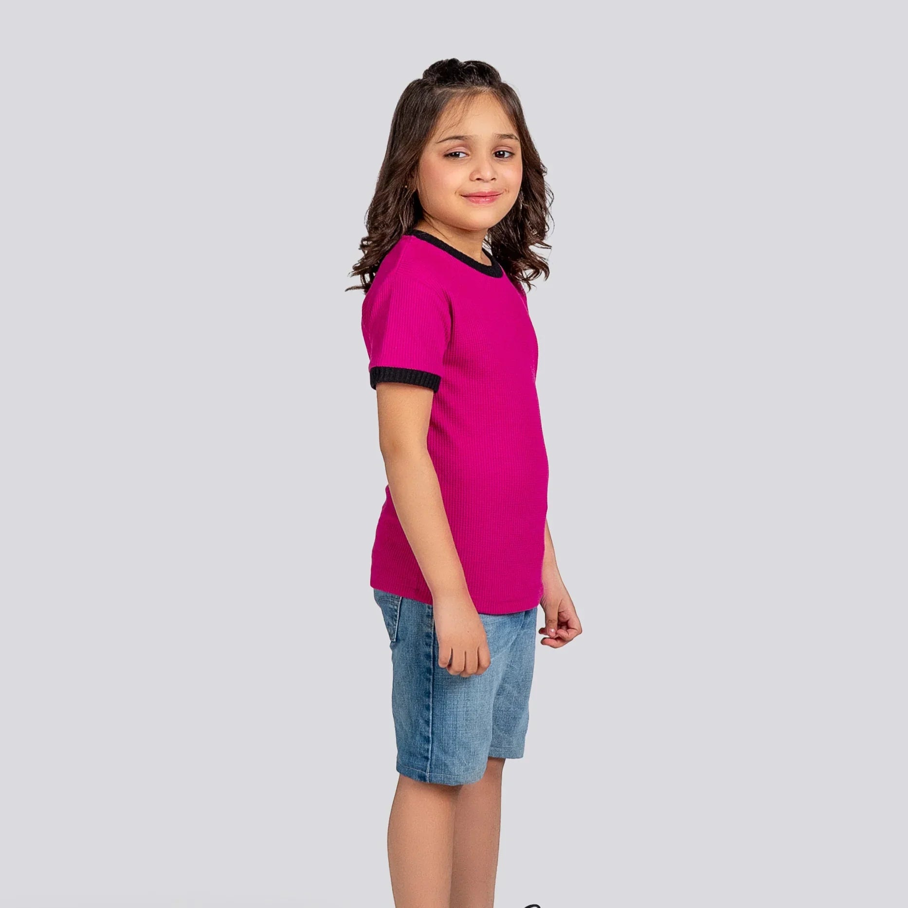 Young girl wearing a pink shirt and blue shorts on a gray background