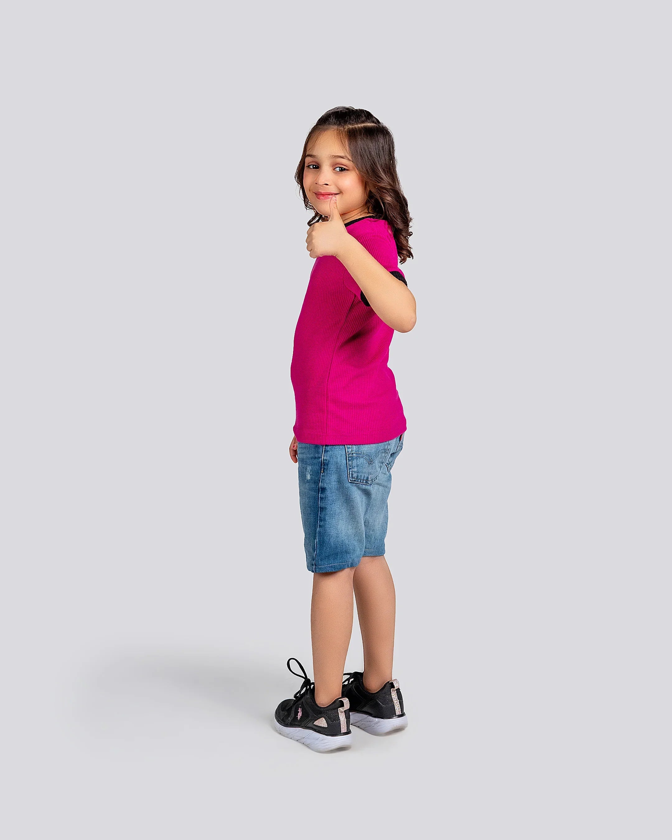 Young girl wearing a pink shirt and denim shorts on a white background