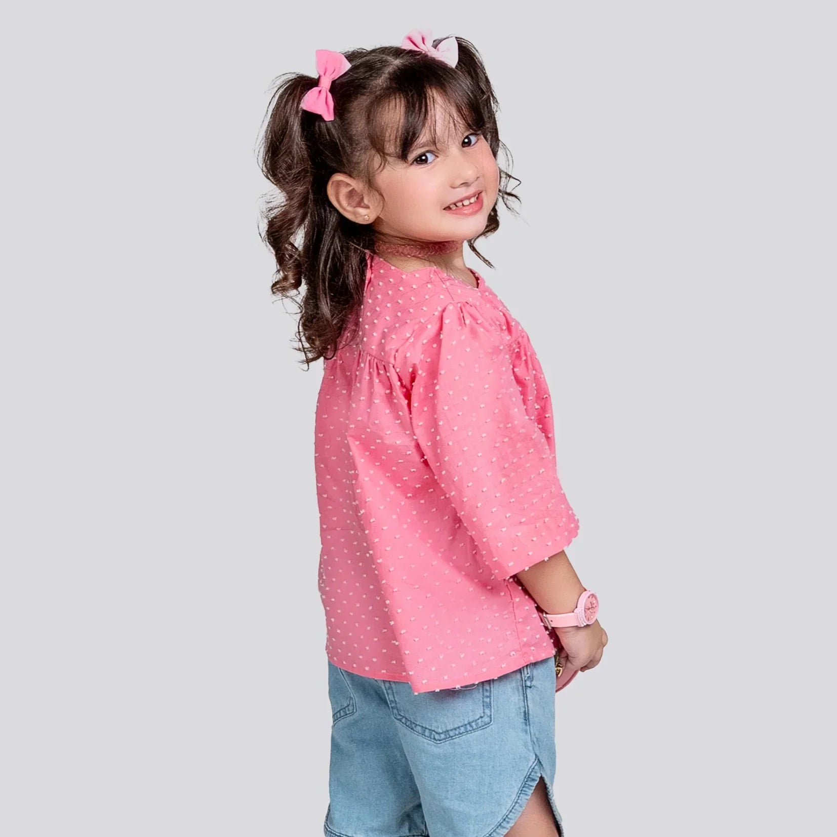Child wearing a pink polka dot shirt and denim shorts on a light gray background
