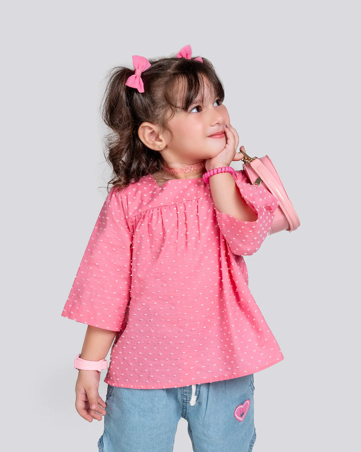 Young girl wearing a pink polka dot blouse and blue jeans on a light gray background