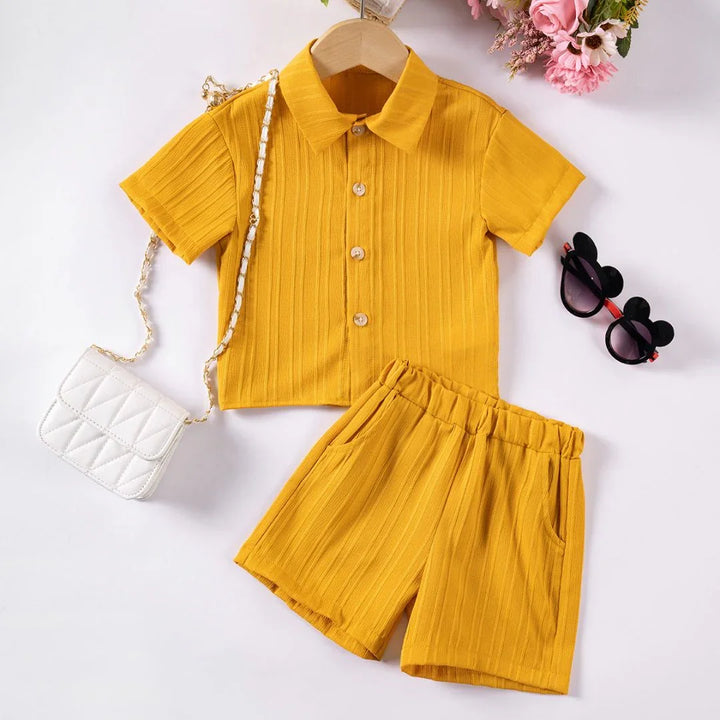 Yellow children's outfit with shorts, white bag, and sunglasses on a white background
