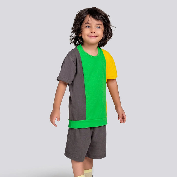 Child wearing a colorful outfit with a green shirt, yellow shorts, and gray sleeves on a light gray background