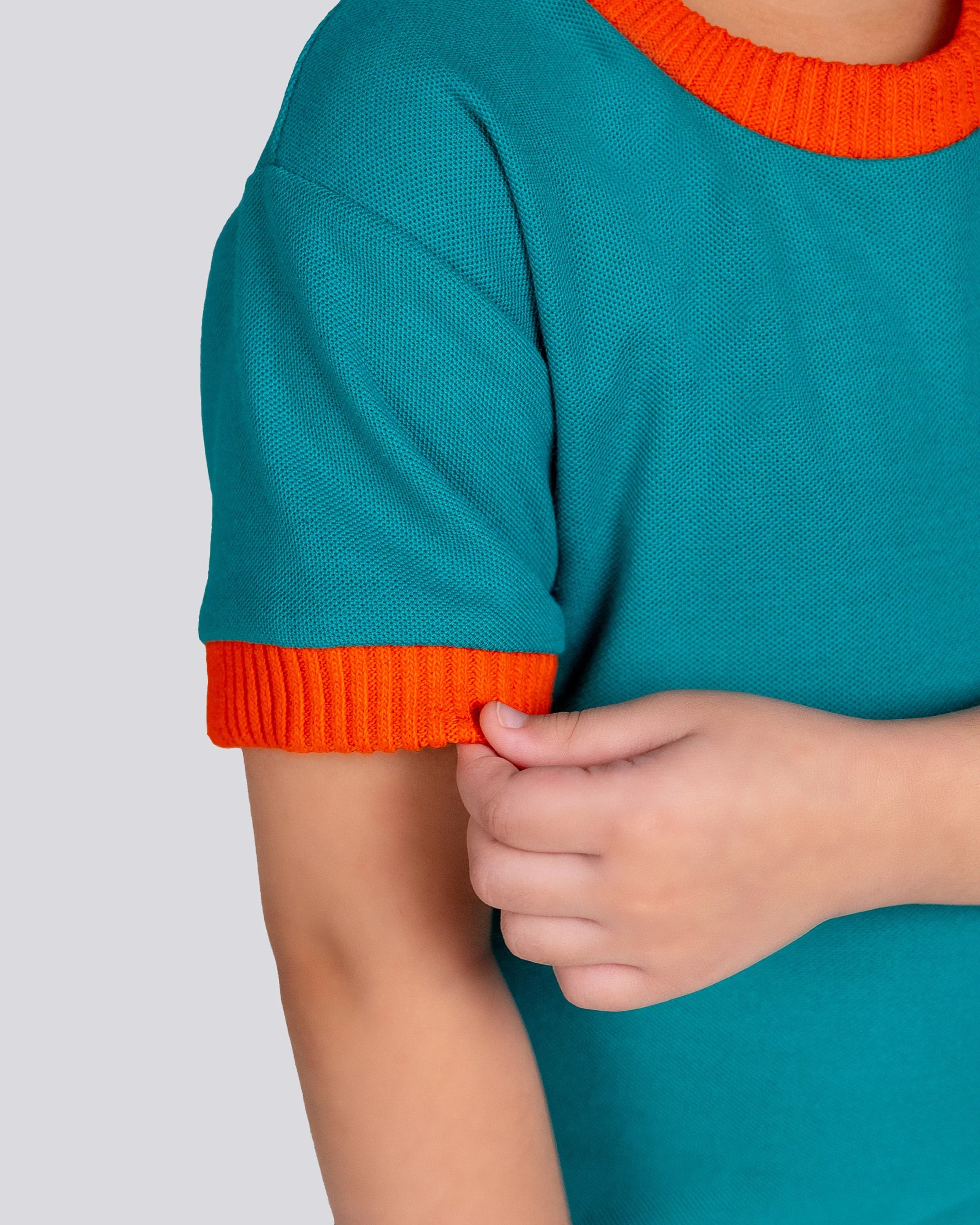 Teal sweater with orange cuffs and hem on a plain background