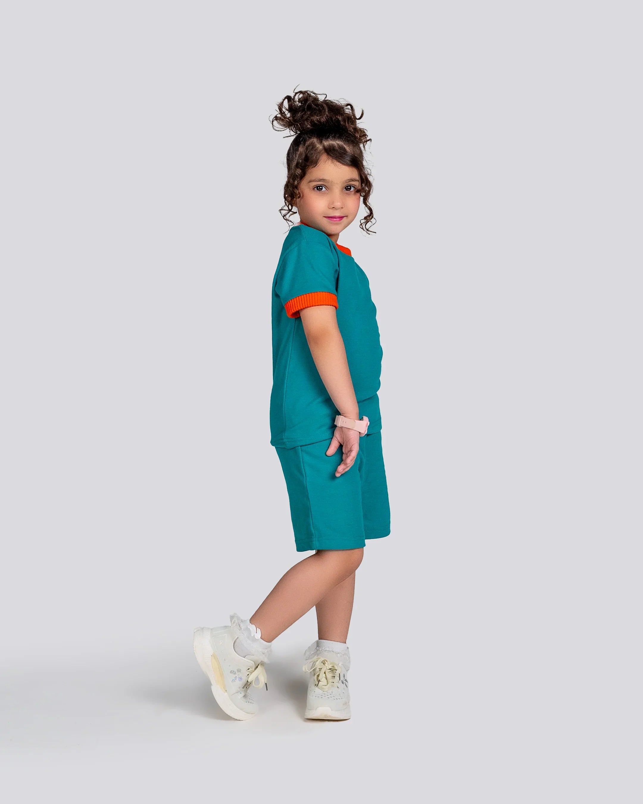 Child wearing a teal outfit with orange trim on a light gray background