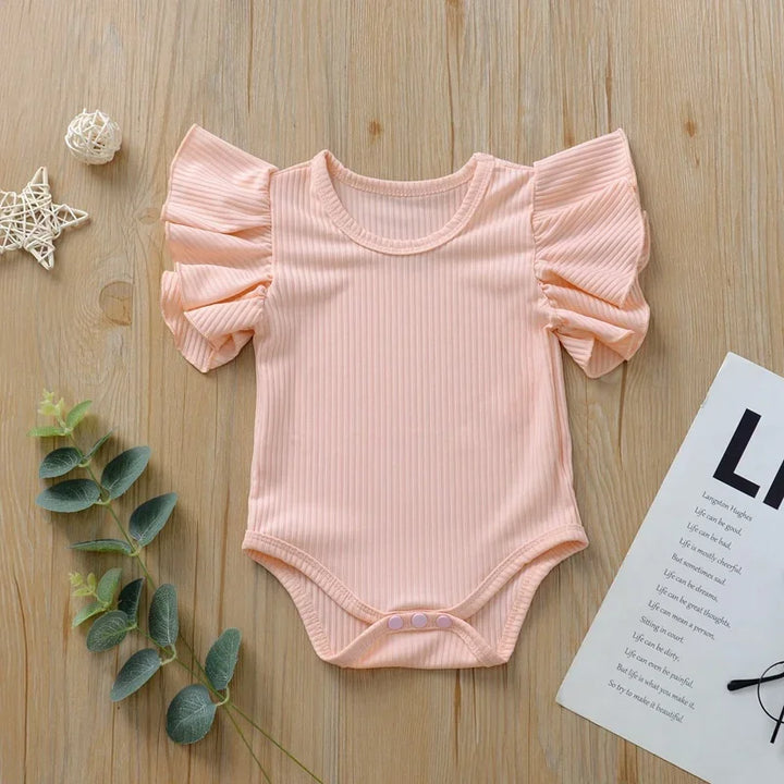 Pink baby bodysuit with ruffled sleeves on a wooden surface with decorative elements.