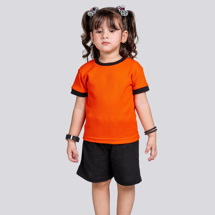 Child wearing an orange shirt and black shorts on a light gray background