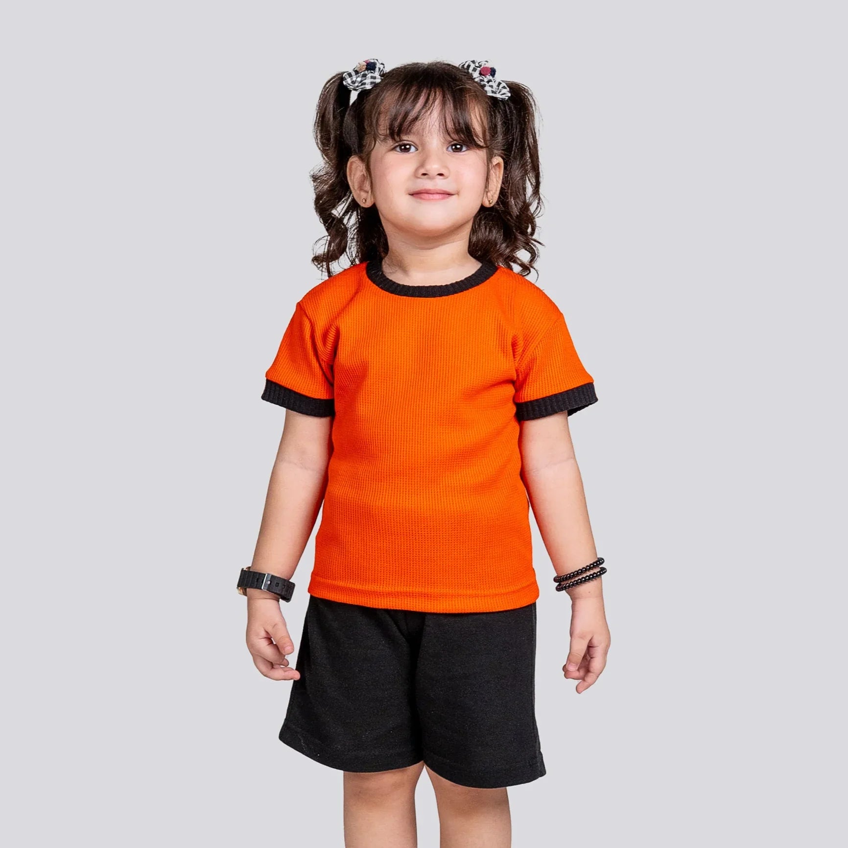 Child wearing an orange shirt and black shorts on a light gray background
