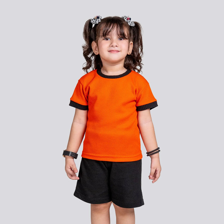 Child wearing an orange shirt and black shorts on a light gray background
