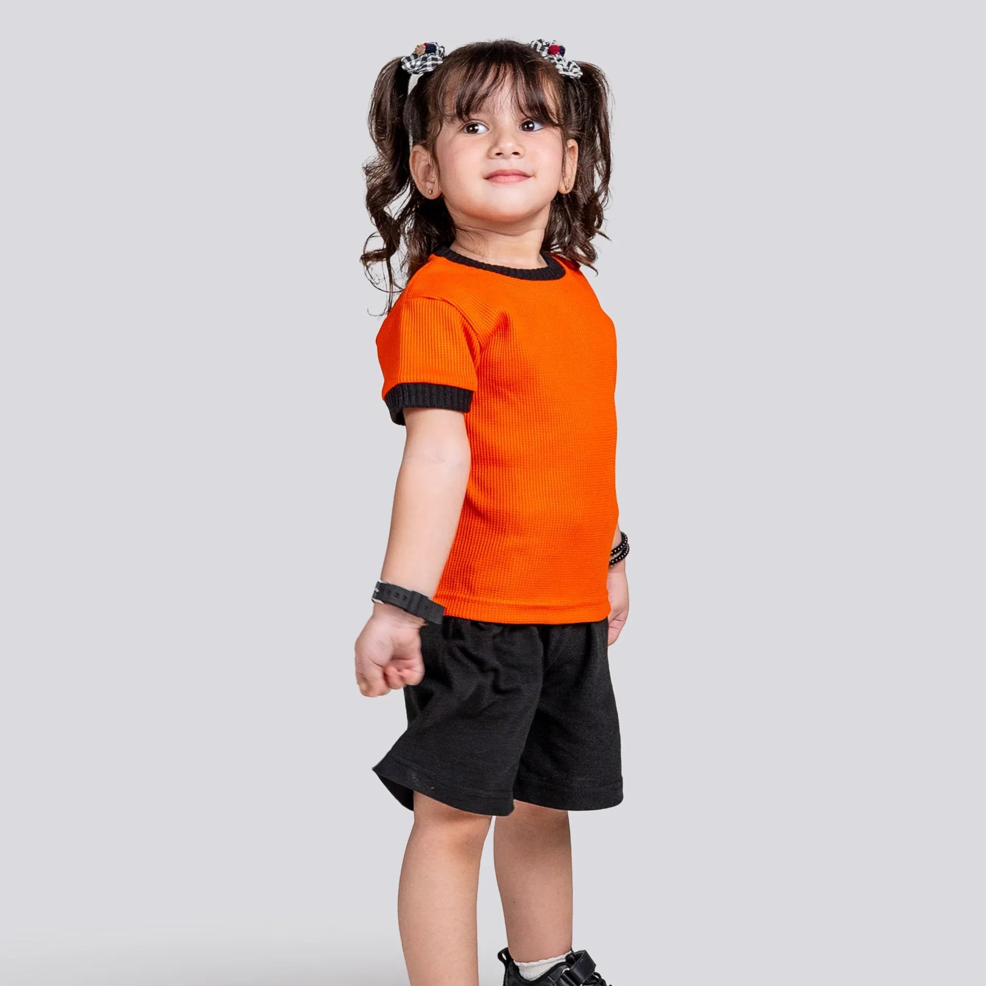 Child wearing an orange shirt and black shorts on a light gray background