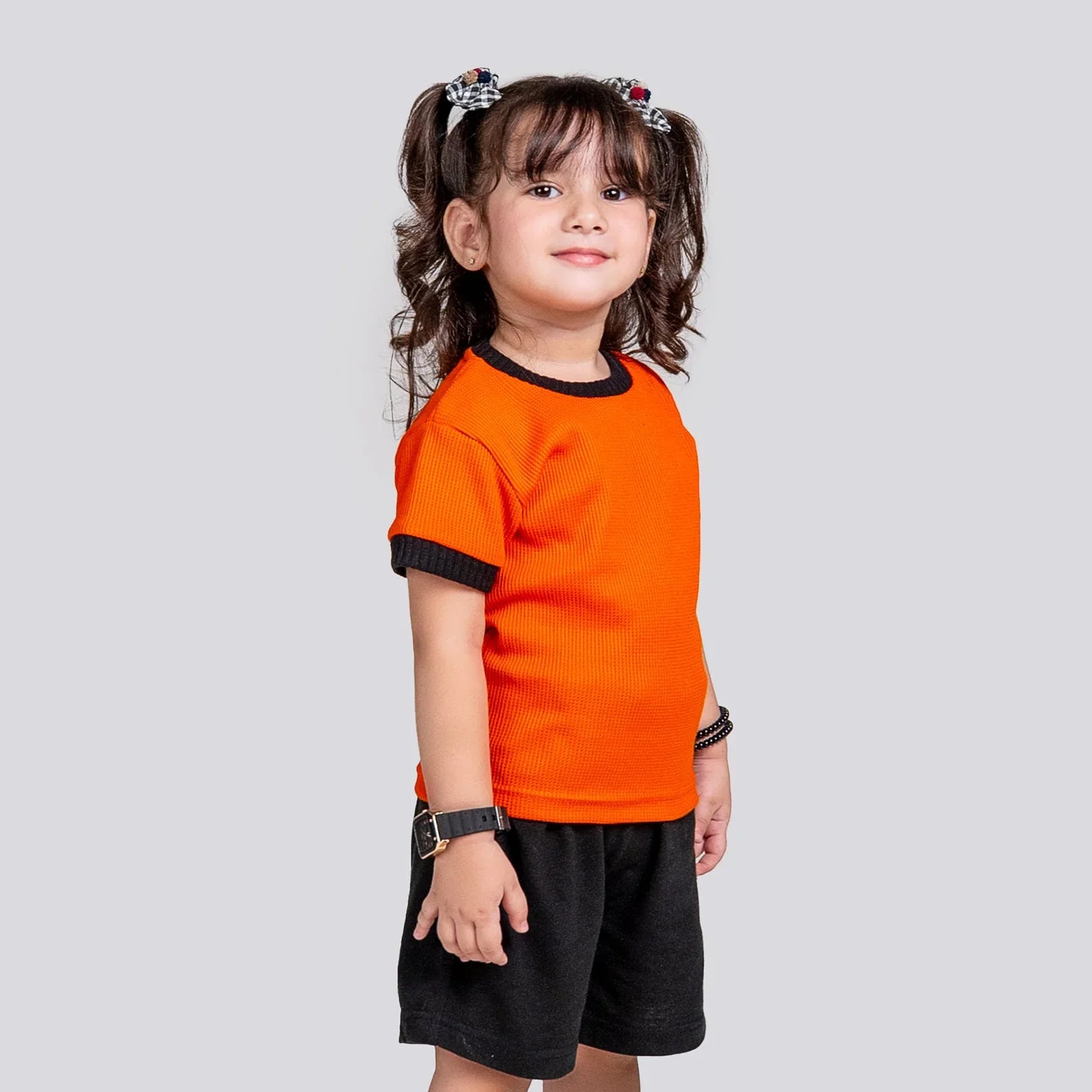 Child wearing an orange shirt and black shorts on a gray background