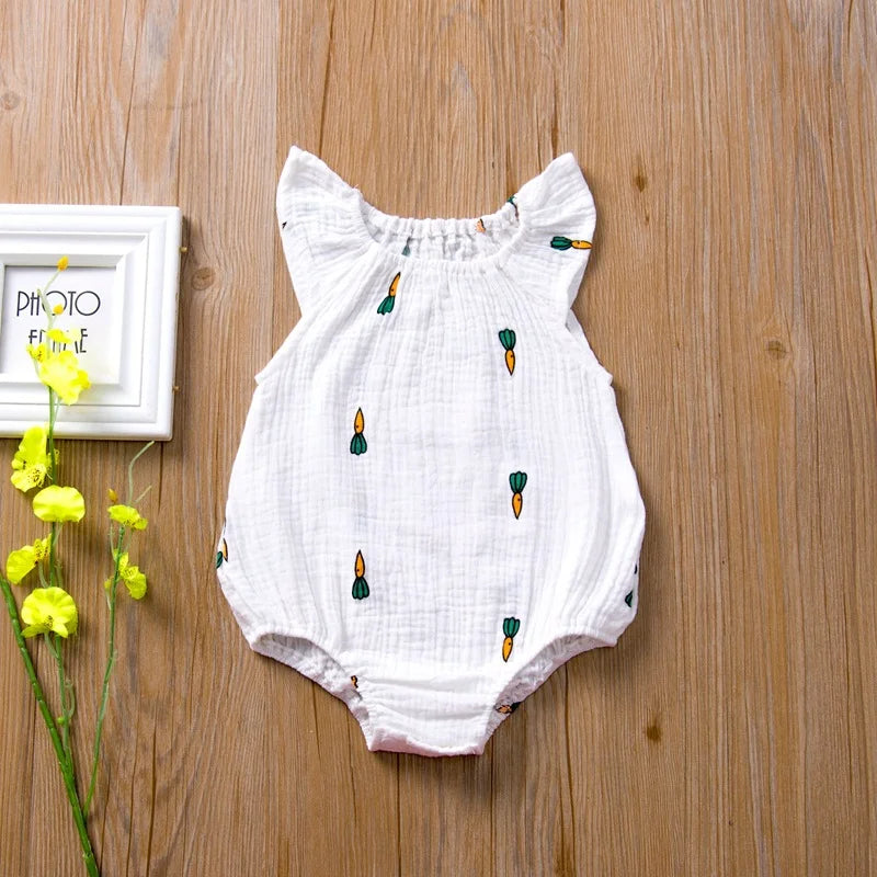 White baby romper with green carrot prints on a wooden surface with yellow flowers and a white frame.