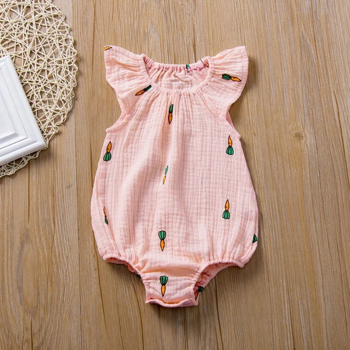 Pink baby romper with embroidered designs on a wooden surface