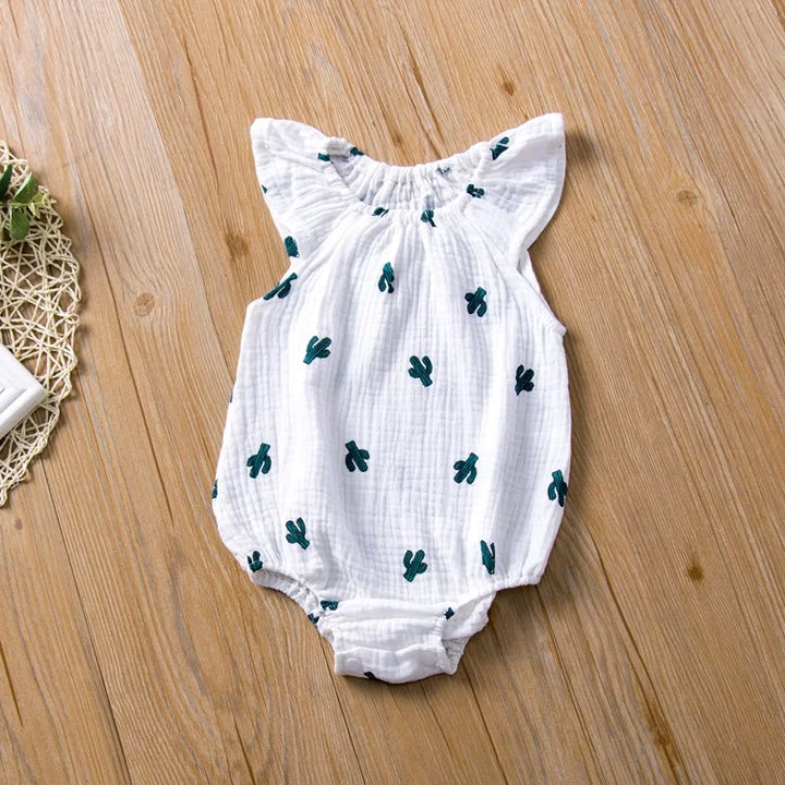 White baby romper with green cactus patterns on a wooden floor
