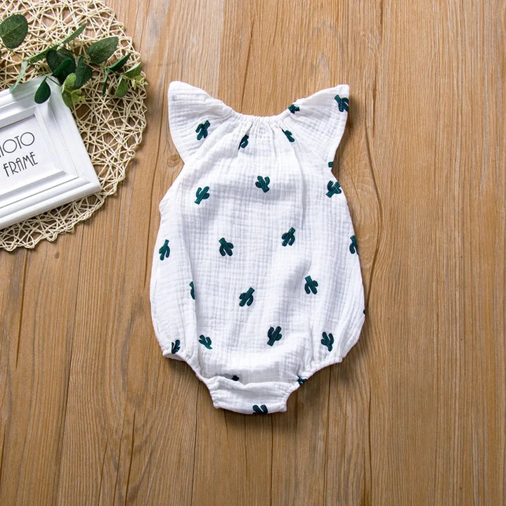White baby romper with green patterns on a wooden surface