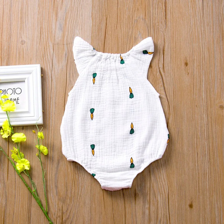 White baby romper with embroidered designs on a wooden surface with flowers.