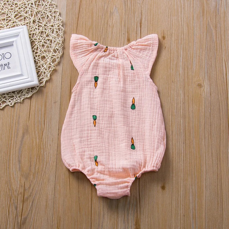 Pink baby romper with embroidered designs on a wooden surface