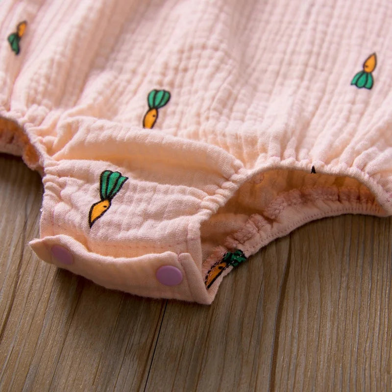 Close-up of a pink textured fabric with embroidered carrot designs on a wooden surface