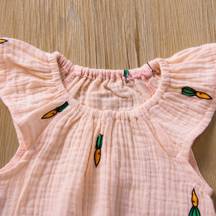 Pink baby dress with embroidered designs on a wooden surface