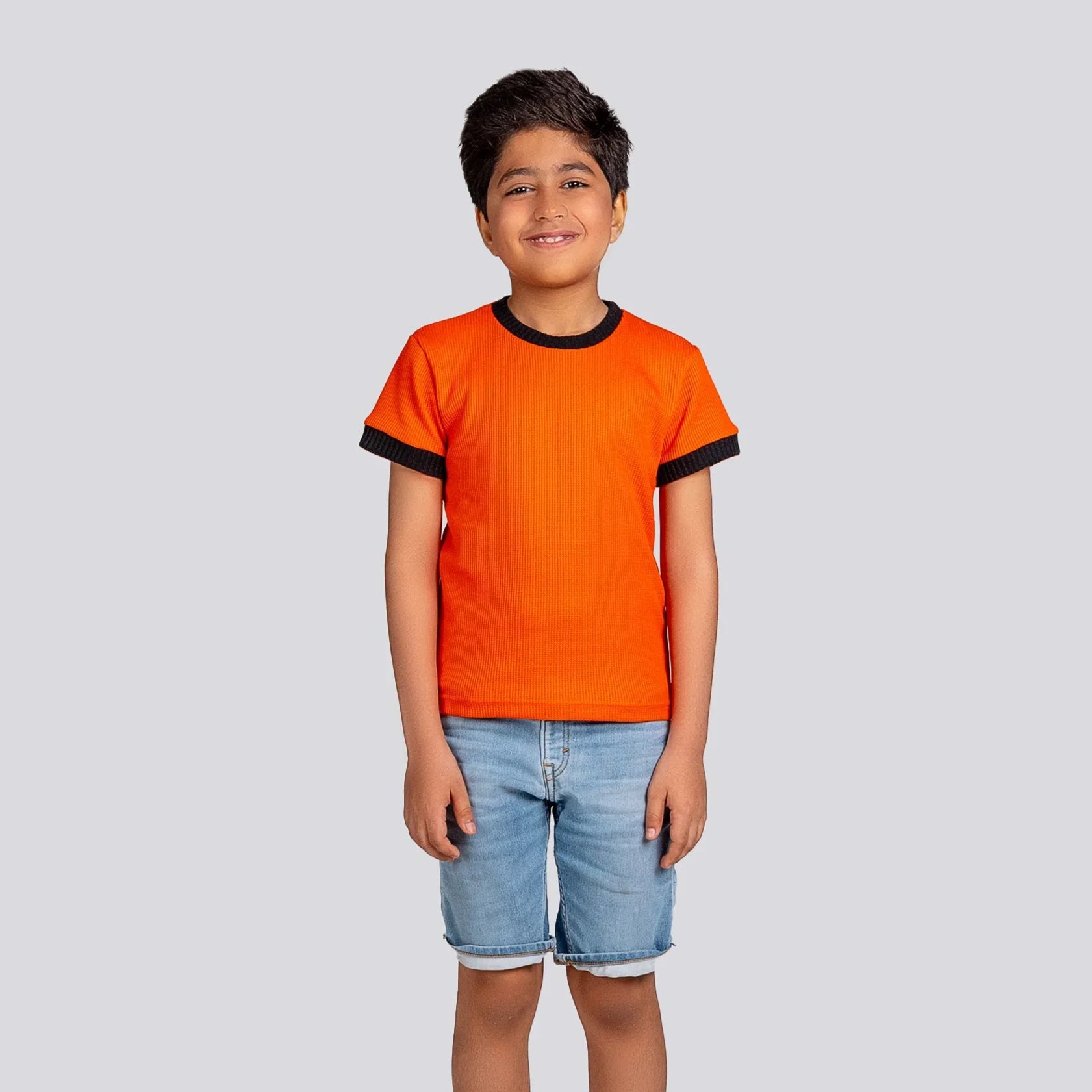 Child wearing an orange t-shirt with black trim and denim shorts on a light gray background