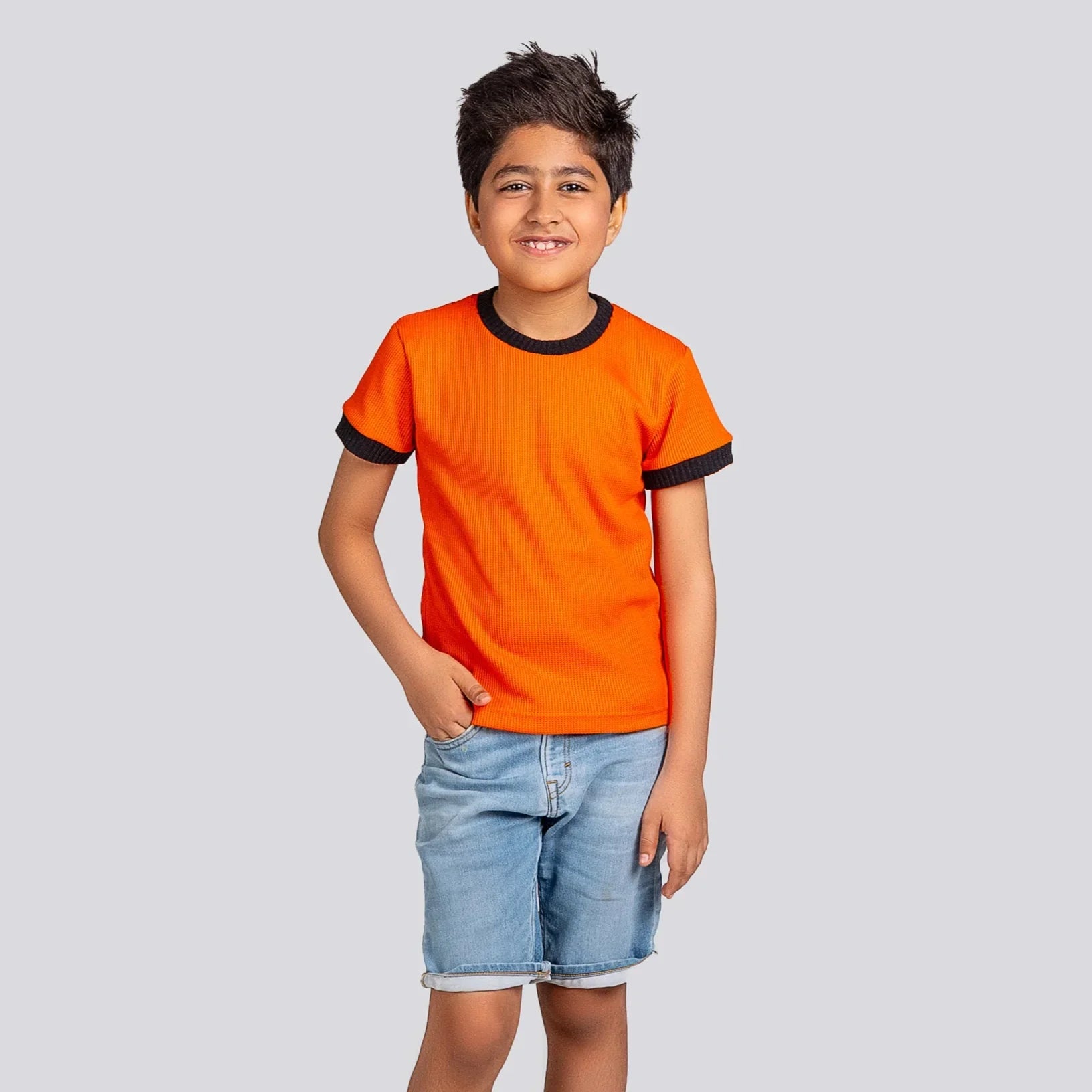 Child wearing an orange t-shirt with black trim and denim shorts on a light gray background