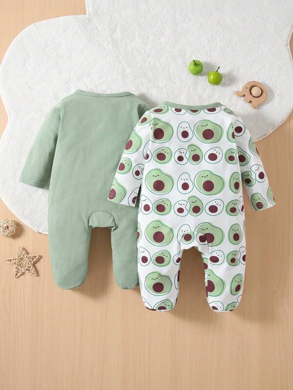 Two baby rompers, one green and one with avocado pattern, on a wooden surface.