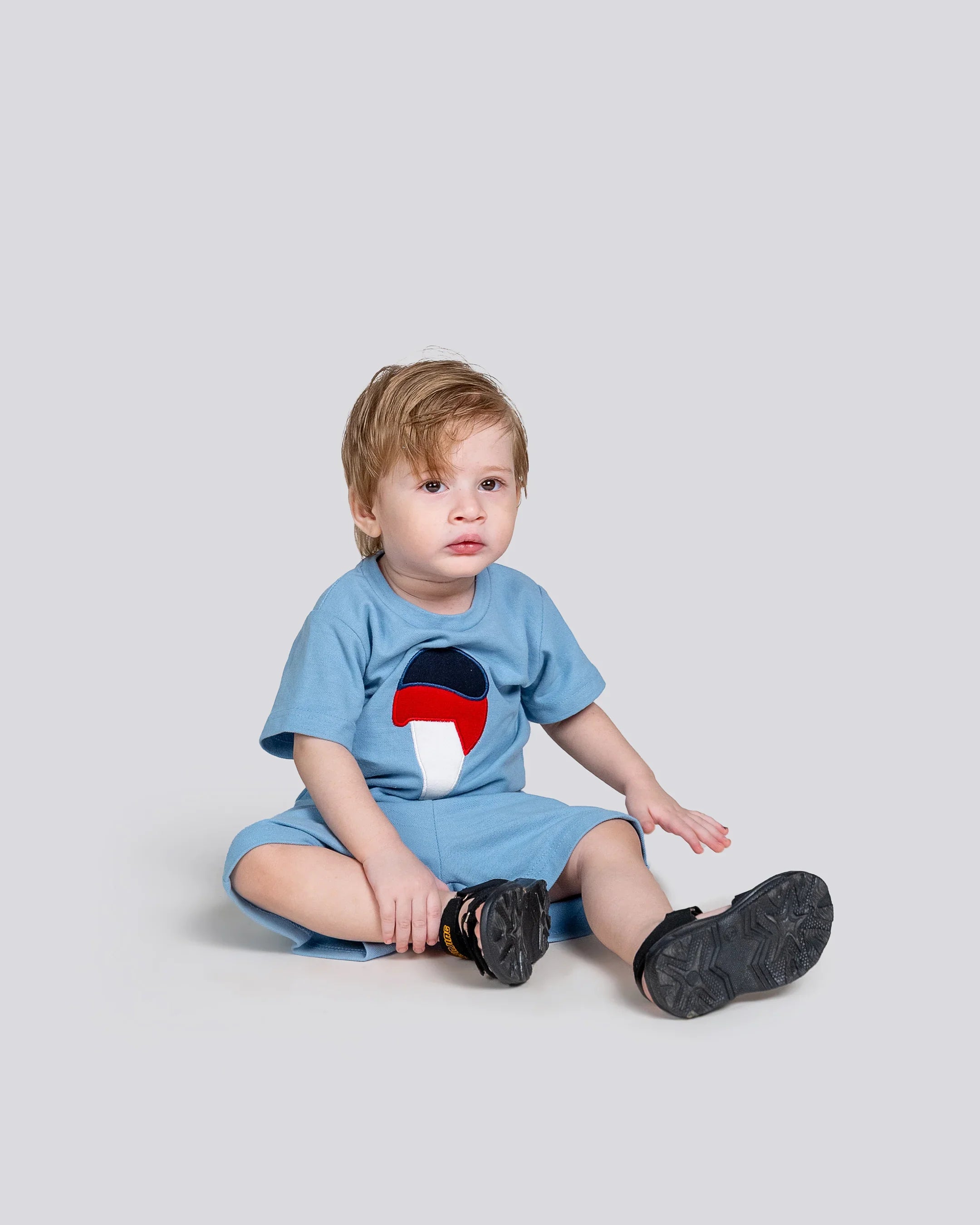 Child wearing a blue outfit with a colorful mushroom design on a light gray background