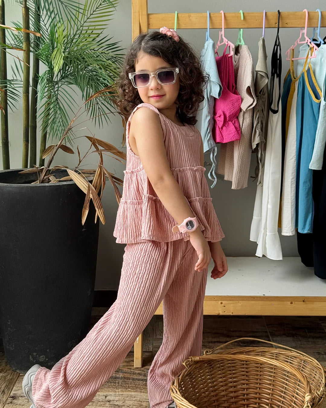 Child in pink outfit standing in a room with clothes on a rack