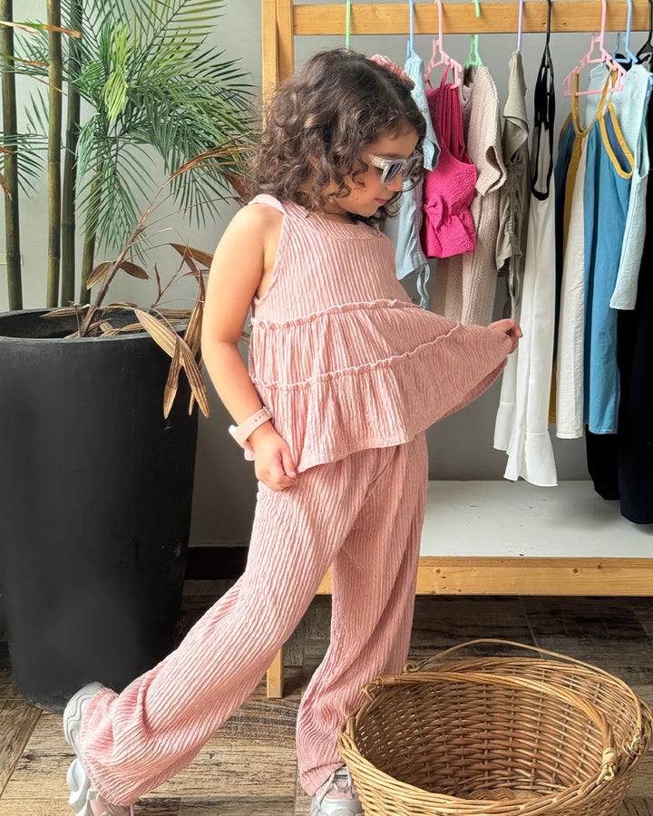 Child in a pink outfit standing in a room with clothes on a rack and a plant.