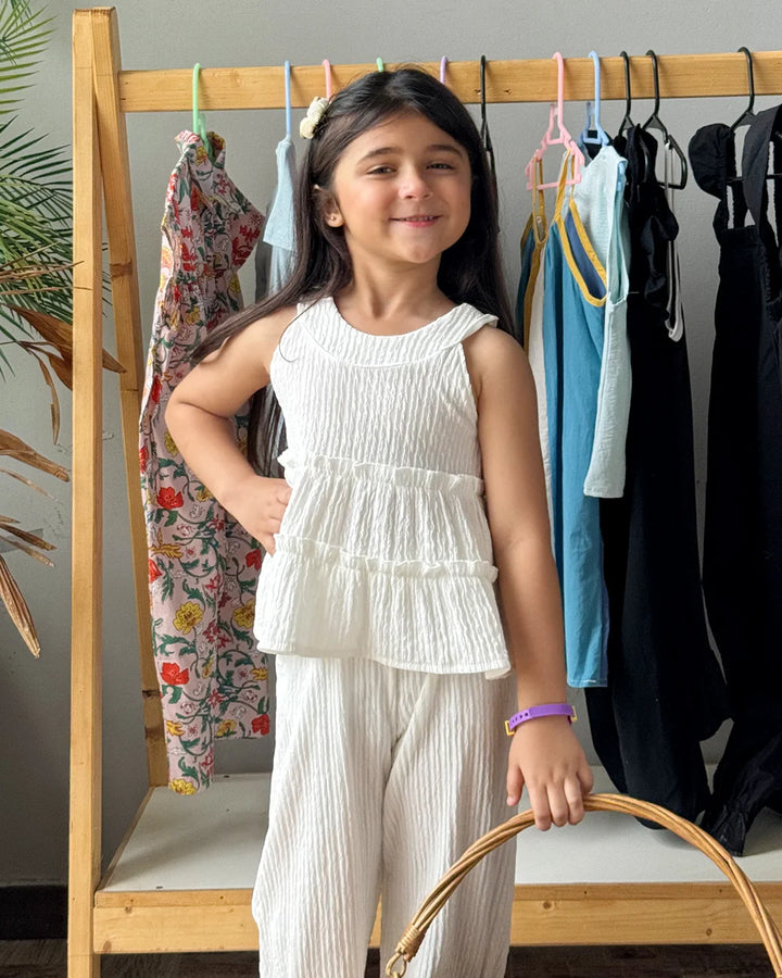 Young girl in a white outfit standing in front of a clothing rack with various garments.