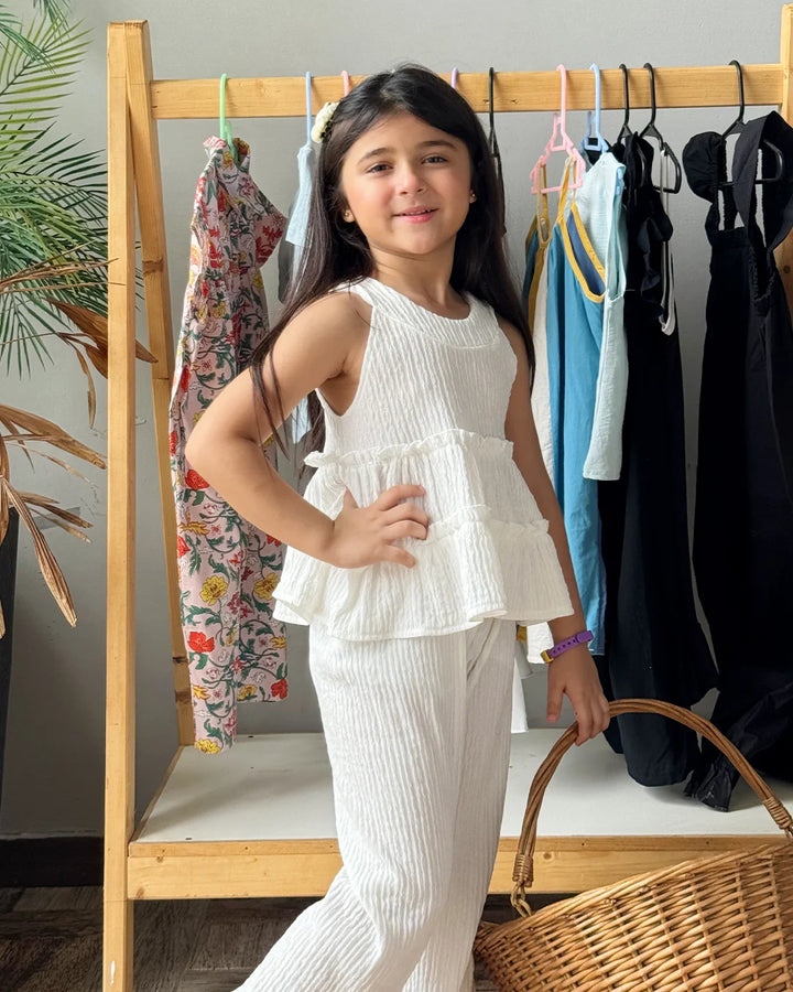 Young girl in a white outfit standing in front of a clothing rack with various garments.