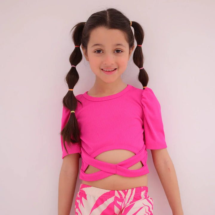 Young girl wearing a bright pink top with cut-out design and matching shorts on a light pink background