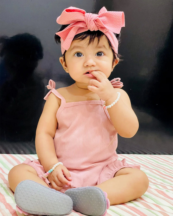 Baby in a pink outfit with a large bow sitting on a striped blanket.