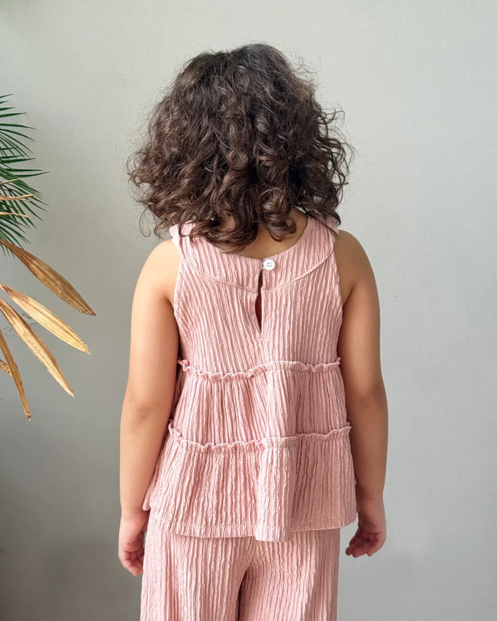 Child wearing a pink textured outfit with a plant in the corner