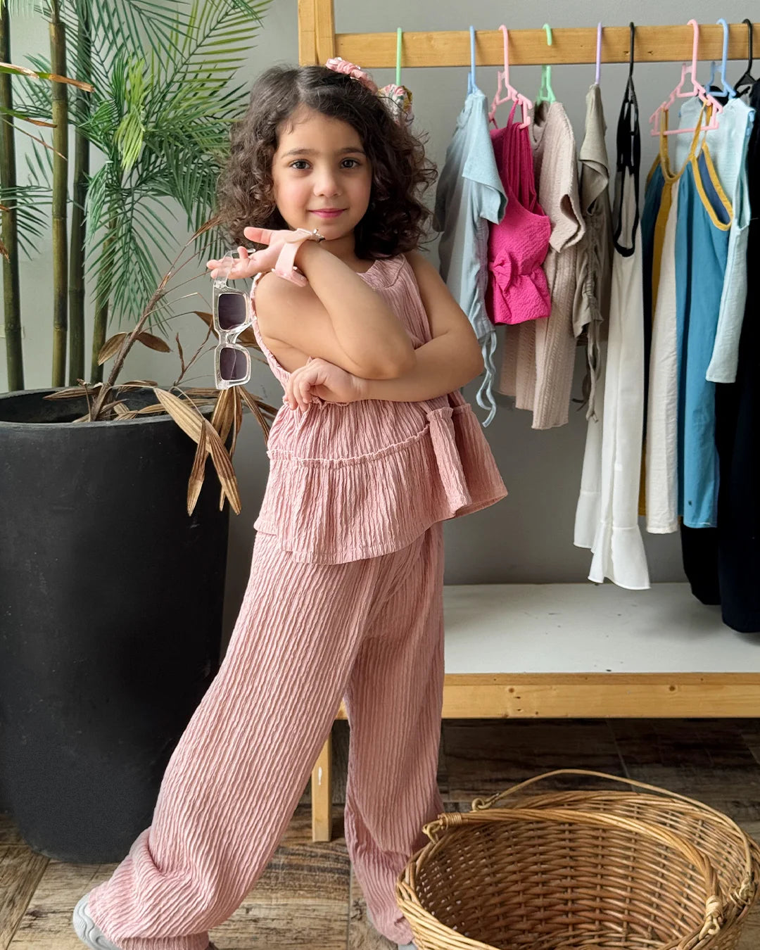 Young girl in a pink outfit standing in front of a clothing rack with various garments.