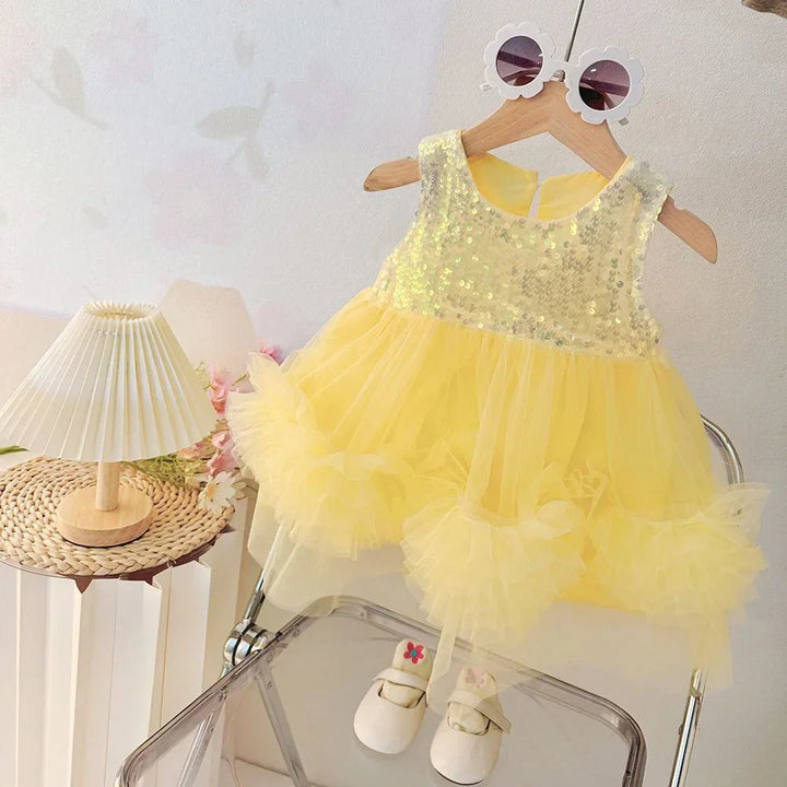 Yellow sequin dress on a hanger with white shoes on a chair, against a light background.