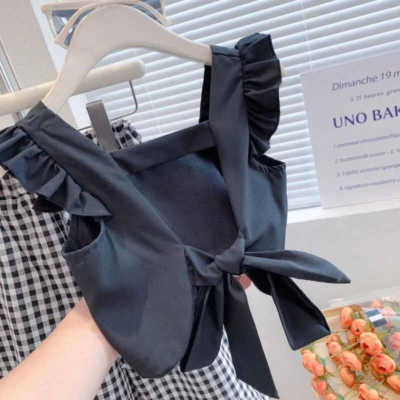 Black top with ruffled details on a hanger in front of a blurred indoor background