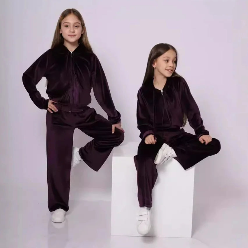 Two children wearing matching dark purple tracksuits on a white background