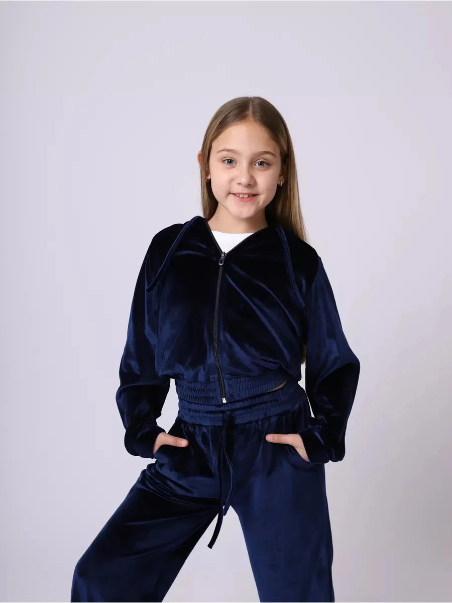 Young girl wearing a navy velvet tracksuit against a white background