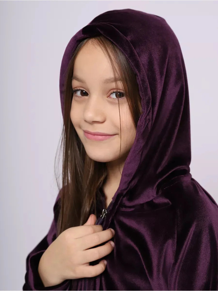 Young girl wearing a purple hooded cloak against a plain background