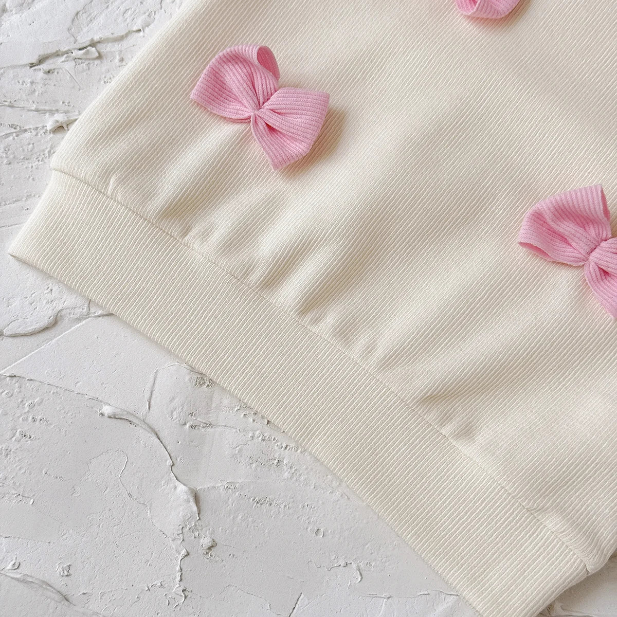 Beige fabric with pink ribbons on a textured white surface