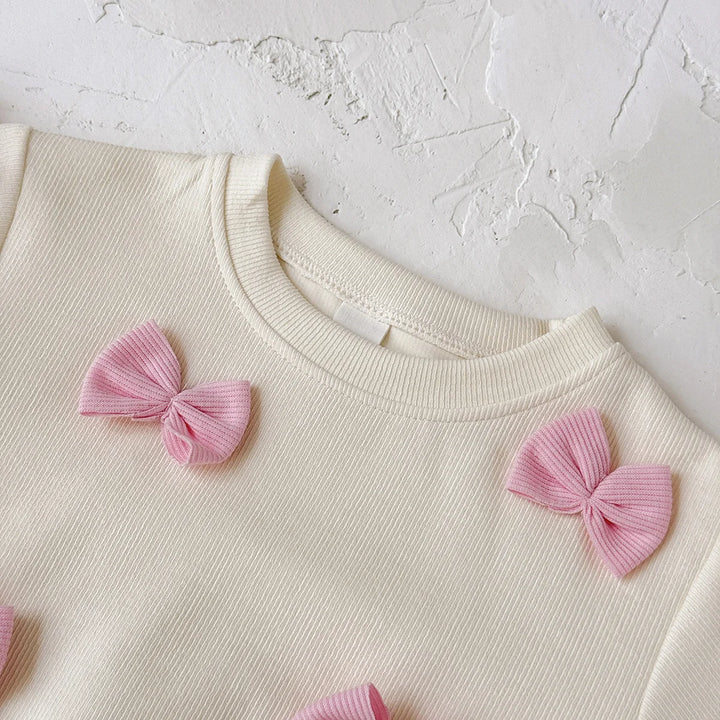 Cream-colored garment with pink bows on a textured white background