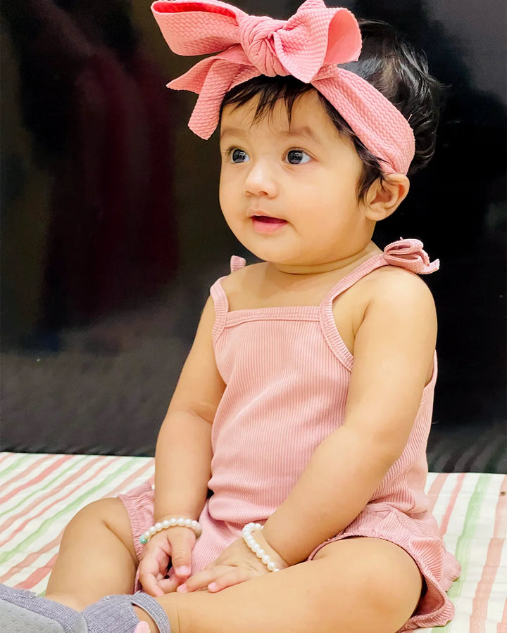 Baby in pink outfit with a large bow sitting on a striped surface
