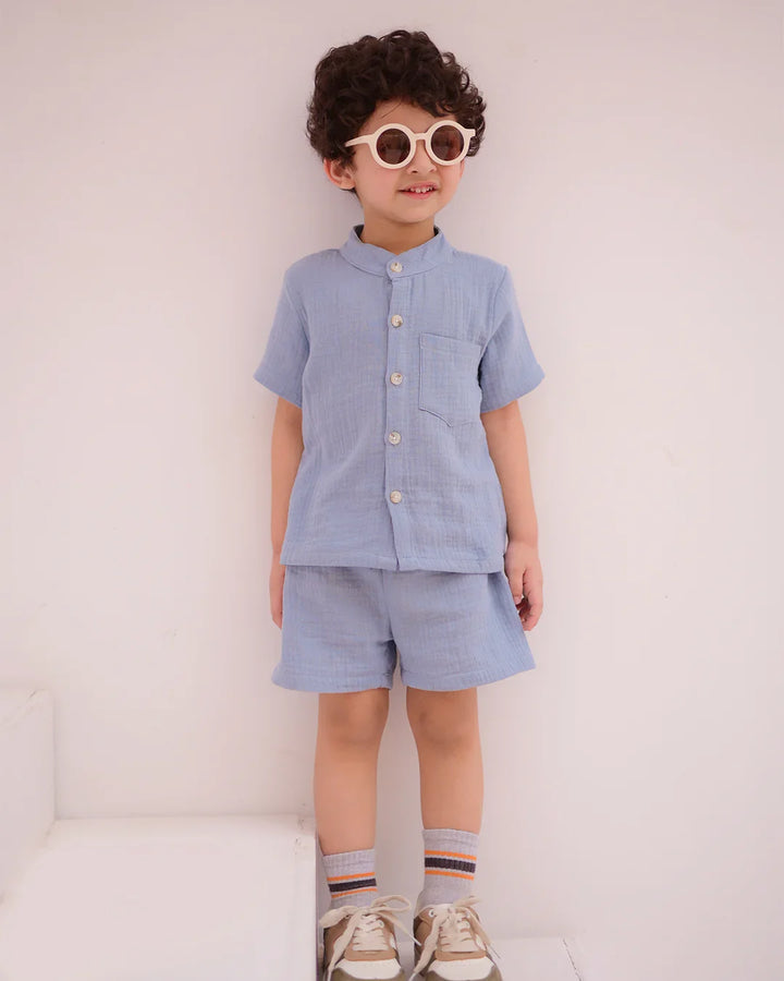 Child wearing a light blue outfit with shorts and a shirt, standing against a white background.
