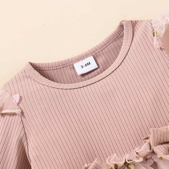 Close-up of a baby pink ribbed sweater with a size label on a beige background