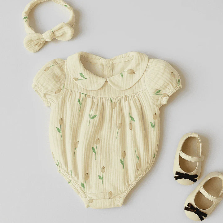 Baby romper with floral pattern, headband, and shoes on a light gray background