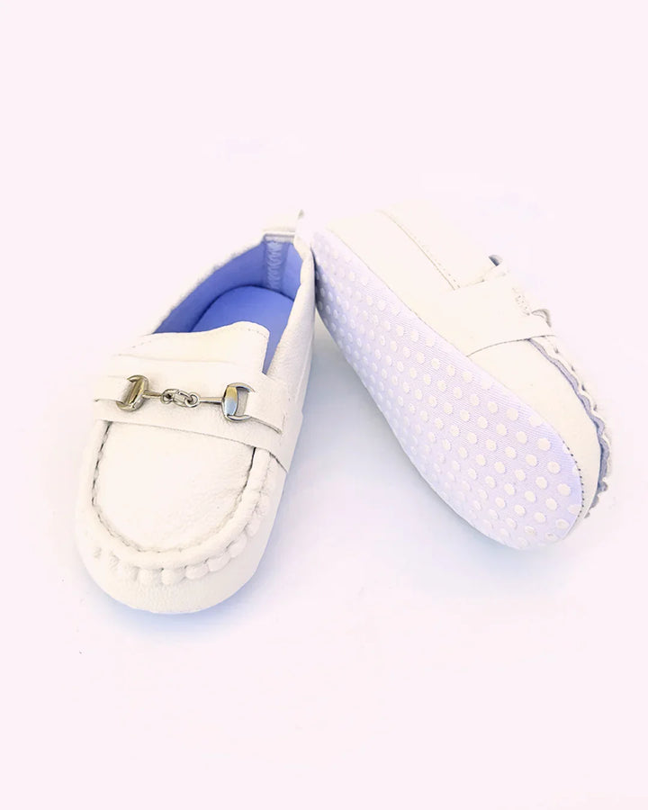 Pair of white loafers with decorative buckle on a light purple background