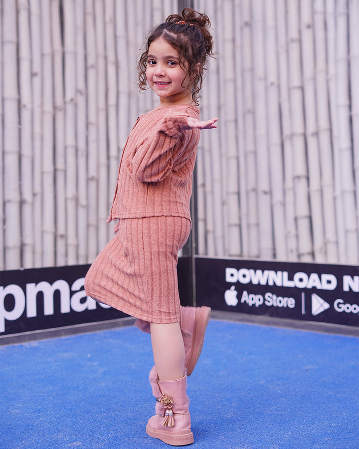 Child in a pink outfit standing on a blue surface with a branded backdrop