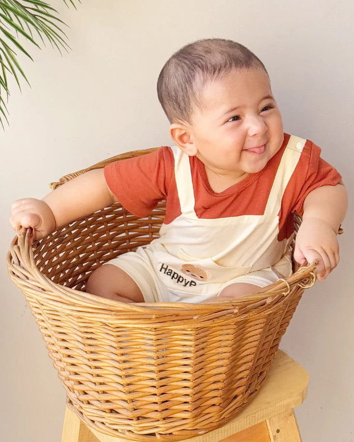 Child wearing a bib with 'Happy' printed on it, sitting inside a woven basket.